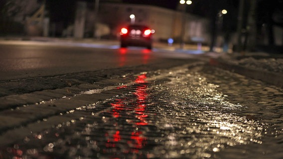 Eine dünne Eisschicht ist auf einer Straße und einem Gehweg im Dunklen zu sehen. © dpa-Bildfunk Foto: Karl-Josef Hildenbrand