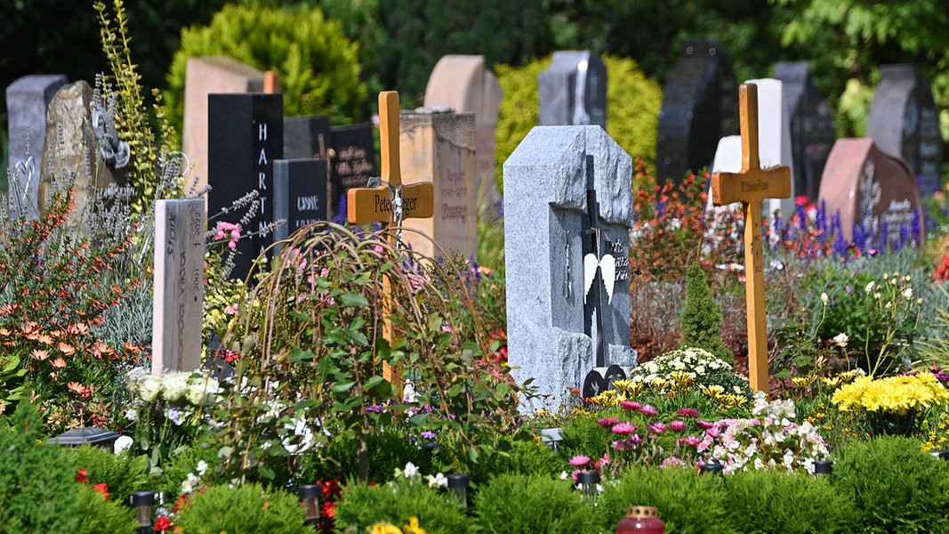 Gräber mit Grabsteinen, Holzkreuzen und vielen geplanzten Blumen auf einem Friedhof. © picture alliance Foto: Sven Simon