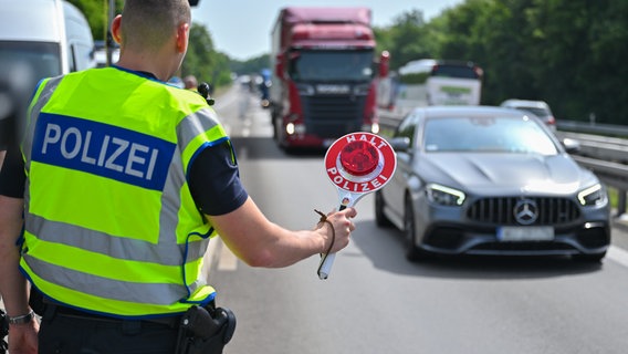Ein Beamter der Bundespolizei steht auf der Autobahn A12 nahe dem deutsch-polnischen Grenzübergang und stoppt ein Auto mit polnischen Fußballfans, die unterwegs nach Berlin zum EM-Spiel Polen gegen Österreich sind. © Patrick Pleul/dpa 