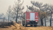 Ein Löschfahrzeug bahnt sich seinen Weg durch abgebrannte Bäume während eines Waldbrandes auf der griechischen Insel Rhodos. © Lefteris Damianidis/InTime News/AP/dpa 