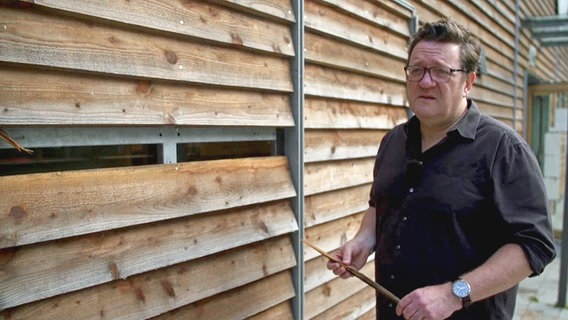 Martin Karolczak, Geschäftsführer GWS St. Pauli, steht nach einem rechten Angriff vor der Holzfassade der Kinder- und Jugendeinrichtung Hexenberg mit einem Stück der Wand in der Hand. © NDR 
