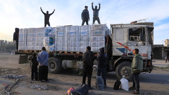 Auf und vor einem mit Hilfsgütern beladenen LKW im Gazastreifen stehen mehrere Menschen. © dpa Bildfunk Foto: Mariam Dagga/AP/dpa