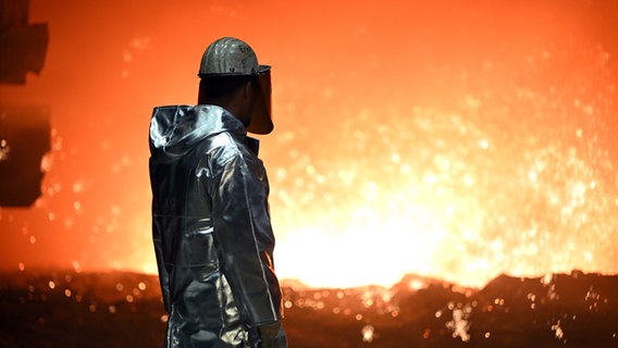 Ein Mann mit Schutzkleidung steht an einem Hochofen und sieht ins Feuer © picture alliance/dpa Foto: Federico Gambarini