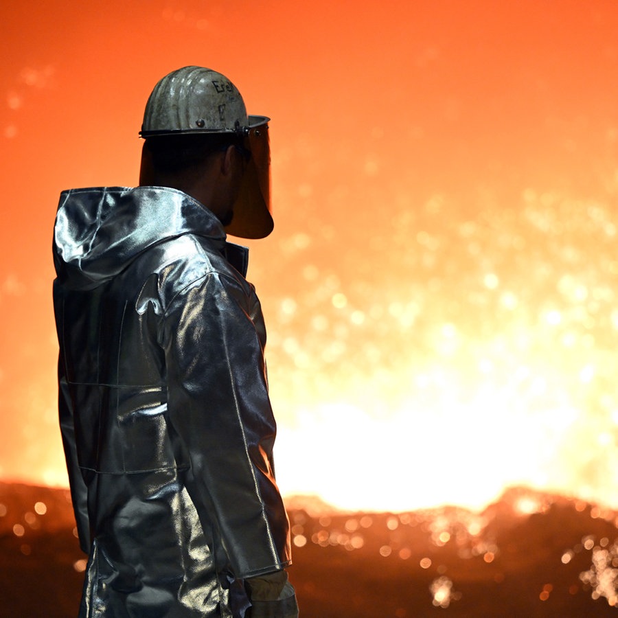 Ein Mann mit Schutzkleidung steht an einem Hochofen und sieht ins Feuer © picture alliance/dpa Foto: Federico Gambarini