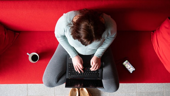 Eine Frau sitzt im Homeoffice auf einer roten Couch und arbeitet an einem Laptop © picture alliance/dpa Foto: Sebastian Kahnert