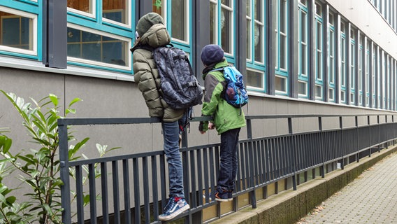 Schüler beobachten vor einem Hamurger Gymnasium ihre Klassenkameraden durch das Fenster. Da Klassenarbeiten in allen Jahrgängen, in denen es um einen Abschluss oder eine Versetzung geht, geschrieben werden, sind einige Schüler in kleinen Gruppen doch in der Schule. Wegen des Corona-Virus bleiben in der Hansestadt alle Schulen und Kitas geschlossen. (Foto vom 16.12.2020) © picture alliance/dpa | Ulrich Perrey 