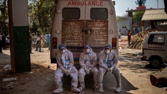 Neu Delhi: Erschöpftes medizinisches Personal, die Opfer, die an den Folgen einer Corona-Infektion verstorben sind, zur Einäscherung bringen, sitzen auf der hinteren Stufe eines Krankenwagens in einem Krematorium. © AP/dpa Foto: Altaf Qadri/AP/dpa