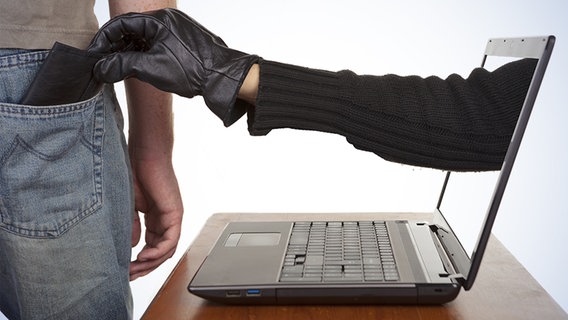 Eine Hand mit Lederhandschuh greift aus einem Laptop an das Portemonnaie in einer Hosentasche. © fotolia.com Foto: davidevison