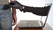 Eine Hand mit Lederhandschuh greift aus einem Laptop an das Portemonnaie in einer Hosentasche. © fotolia.com Foto: davidevison