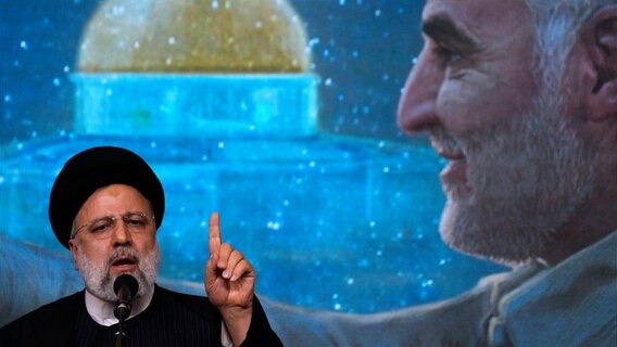 Ebrahim Raisi, Präsident des Iran, spricht während einer Gedenkfeier für den verstorbenen Revolutionsgardengeneral Soleimani, der im Hintergrund auf einem Bildschirm zu sehen ist, in der großen Imam-Khomeini-Moschee. © Vahid Salemi/AP/dpa 