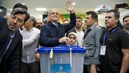 Der reformorientierte Kandidat für die iranischen Präsidentschaftswahlen, Massud Peseschkian, gibt bei der Wahl im Iran seinen Stimmzettel ab, während er den Medien in einem Wahllokal zuwinkt. © dpa bildfunk/Iranian Students' News Agency, ISNA via AP Foto: Majid Khahi