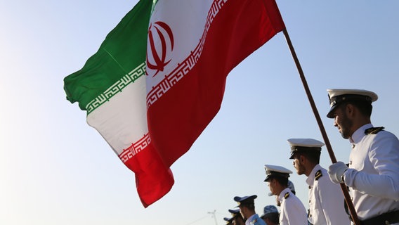 Iranische Soldaten in Gardeuniform schwenken während einer Parade die Staatsfahne. © picture alliance/dpa/ZUMA Press Wire Foto: Rouzbeh Fouladi