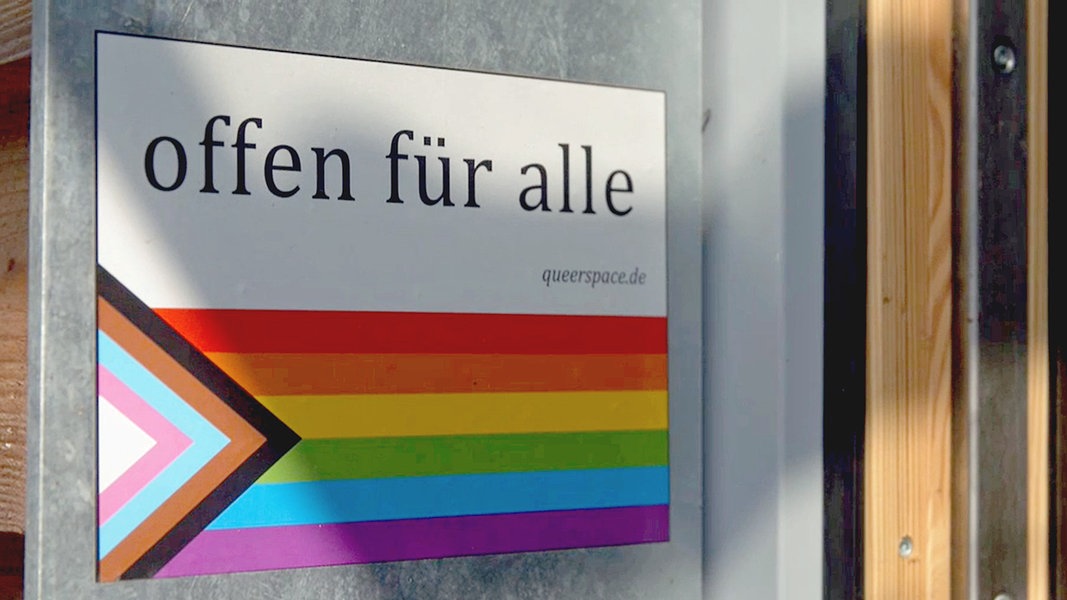 An einer Wand klebt ein Sticker in Regenbogenfarben mit der Aufschrift: 
