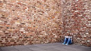 Ein junges Mädchen sitzt mit gesenktem Kopf vor einer hohen Mauer. © photocase.de Foto: Mr. Nico