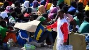 Migranten stehen in einem Aufnahmezentrum für Migranten. Der Stadtrat der italienischen Mittelmeerinsel Lampedusa hat angesichts Tausender neu angekommener Bootsmigranten den Notstand ausgerufen. © dpa Foto: Valeria Ferraro