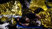Eine Frau und ein Kind schlafen vor dem Aufnahmezentrum für Migranten. Der Stadtrat der italienischen Mittelmeerinsel Lampedusa hat angesichts Tausender neu angekommener Bootsmigranten den Notstand ausgerufen. © dpa Foto: Valeria Ferraro