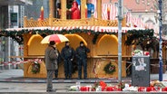 Ein Passant mit Regenschirm und Polizisten stehen vor dem geschlossenen Weihnachtsmarkt in Magdeburg. © dpa Foto: Sebastian Kahnert