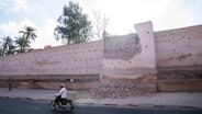 Marokko, Marrakesch: Ein Mann fährt nach einem Erdbeben an einer beschädigten Mauer der historischen Medina vorbei. © Mosa'ab Elshamy/AP/dpa 