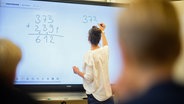 Eine Lehrerin schreibt eine Mathematikaufgabe auf eine digitale Schultafel im Klassenraum einer 4. Klasse einer Grundschule in der Region Hannover. © Julian Stratenschulte/dpa 