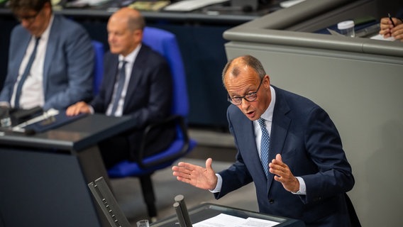 Unionsfraktionschef Friedrich Merz (CDU) spricht im Bundestag - im Hintergrund, leicht unscharf, Bundeskanzler Olaf Scholz (SPD). © Michael Kappeler/dpa Foto: Michael Kappeler/dpa