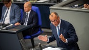 Unionsfraktionschef Friedrich Merz (CDU) spricht im Bundestag - im Hintergrund, leicht unscharf, Bundeskanzler Olaf Scholz (SPD). © Michael Kappeler/dpa Foto: Michael Kappeler/dpa