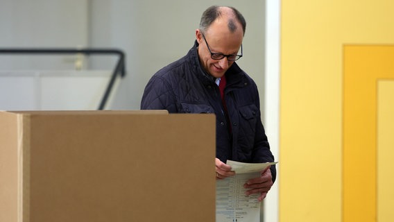 Friedrich Merz (CDU) geht im Wahllokal in der Schützenhalle Arnsberg-Niedereimer mit seinem Wahlzettel zu einer Wahlkabine. © dpa Foto: Rolf Vennenbernd