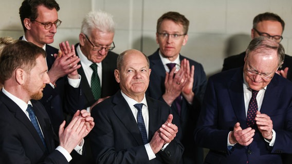 Michael Kretschmer (CDU, l-r), Ministerpräsident von Sachsen, Hendrik Wüst (CDU), Ministerpräsident von Nordrhein-Westfalen, Winfried Kretschmann (Bündnis 90/Die Grünen), Ministerpräsident von Baden-Württemberg, Olaf Scholz (SPD), Bundeskanzler, Daniel Günther (CDU), Ministerpräsident von Schleswig-Holstein, Stephan Weil (SPD), Ministerpräsident von Niedersachsen, und Mario Voigt (CDU), Ministerpräsident von Thüringen, klatschen nach der Unterzeichnung des Finanzierungsabkommens der Stiftung Preußischer Kulturbesitz während der Ministerpräsidentenkonferenz im Bode-Museum. © Hannes P. Albert/dpa 