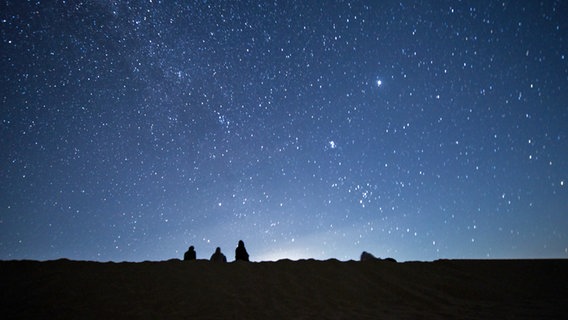 Mehrere Menschen beobachten in der Nacht die Milchstraße. © dpa Foto: Sayed Hassan