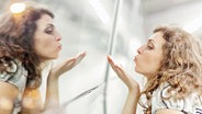 Eine Frau wirft ihrem eigenen Spiegelbild eine Kusshand zu. © picture alliance / imageBROKER | rgb fotografie 