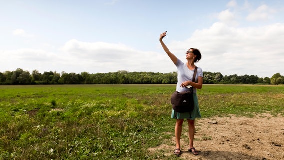 Eine Frau sucht in ländlicher Umgebung mit ihrem Handy nach einem Netzempfang © picture alliance / Caro Foto: Geilert