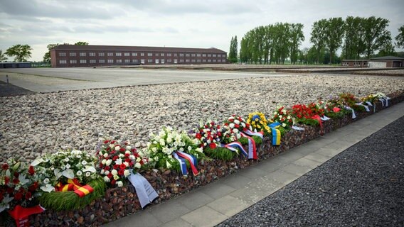 Im Gedenken des Kriegsendes und der Befreiung der Häftlinge des ehemaligen Konzentrationslagers Neuengamme liegen Blumenkränze in der Gedenkstätte. Dahinter sind mit Steinen gefüllte Drahtkörbe zu sehen, welche die Stelle der ehemaligen Holzbaracken der Häftlinge markieren. (Foto vom 3.5.2023) © Gregor Fischer/dpa 