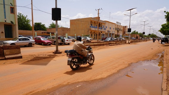 Ein Motorradfahrer fährt auf einer staubigen Straße in Niger. © picture alliance Foto: Sam Mednick