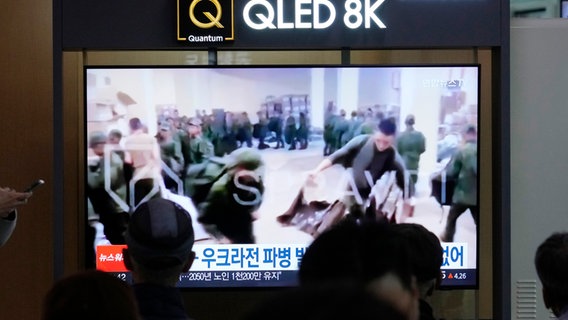 In einer Nachrichtensendung auf einem Fernsehbildschirm am Bahnhof sind Soldaten zu sehen, die vermutlich aus Nordkorea stammen und bereitstehen, um Nachschub aus Russland zu erhalten. © Ahn Young-joon/AP/dpa 