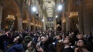 Menschen blicken auf, als die Orgel in der Kathedrale Notre Dame während der ersten öffentlichen Messe zu spielen beginnt. © Michel Euler/AP 