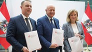 Die österreichischen Parteivorsitzenden Christian Stocker von der ÖVP, Andreas Babler von der SPÖ und Beate Meinl-Reisinger von den NEOS posieren mit ihrem Regierungsprogramm nach einer Pressekonferenz zur Bildung einer Koalitionsregierung. © dpa-Bildfunk Foto: Heinz-Peter Bader