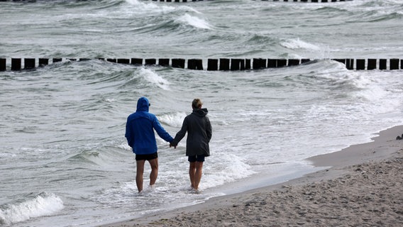 Spaziergänger sind bei Wind an einem Ostseestrand spazieren. © picture alliance/dpa | Bernd Wüstneck 