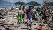 Dorfbewohner wandern durch Trümmer nach den Erdbeben und dem Tsunami in Palu. © Wire/dpa Foto: Ivan Damanik/ZUMA