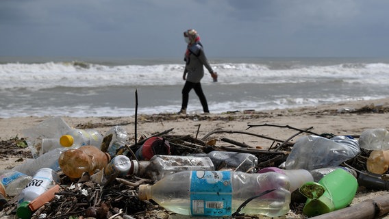 Eine Frau geht an einem Strand entlang, an dem Plastikmüll angespült wurde. © picture alliance/dpa/BERNAMA Foto: Mohd Khairul Fikiri Osman