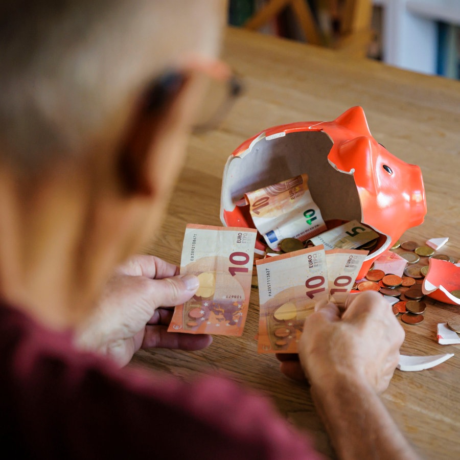 Ein alter Mann sitzt zu Hause am Tisch vor einem zerbrochenen Sparschwein und zählt Geld. © picture alliance Foto: Thomas Trutschel