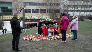 Personen stehen am "Blauen Klavier", auf dem zahlreiche Kerzen und Blumen zum Gedenken an die Opfer der tödlichen Messerattacke vom 22.01.2025 abgelegt wurden. © dpa Foto: Daniel Vogl