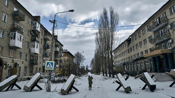 Ein ukrainischer Soldat geht eine Straße in Bachmut entlang, auf der Panzersprerren stehen. © Libkos/AP/dpa 