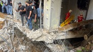 Menschen und Rettungskräfte versammeln sich am Ort eines israelischen Raketeneinschlags in den südlichen Vororten von Beirut (Libanon). © AP Foto: Bilal Hussein