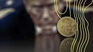 Ein symbolischer Bitcoin vor Donald Trumps Gesicht. © picture alliance Foto: Pablo Gianinazzi