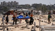 Palästinenser tragen eine der Leichen, die von Israel zurückgebracht wurde, auf einen Friedhof in Chan Junis. © AP/dpa Foto: Abdel Kareem Hana