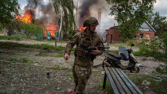 Ein Polizist läuft vor einem brennenden Haus, das durch einen russischen Luftangriff zerstört wurde. © picture alliance/dpa/AP | Evgeniy Maloletka Foto: Evgeniy Maloletka