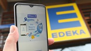 Ein Mann hält vor einer Filiale von Edeka ein Smartphone in der Hand, auf dem die App von Payback aufgerufen wurde. Ab 2025 kooperieren Edeka und das Bonuspunkte-Programm. © imago images Foto: Hanno Bode