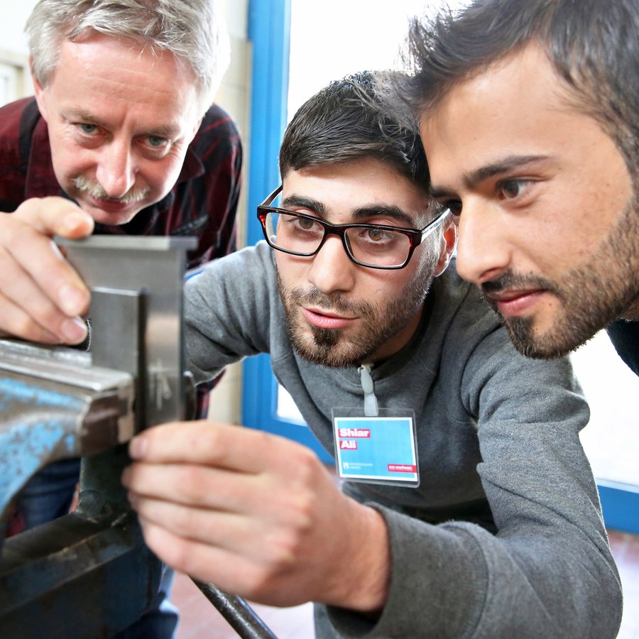 Ein Ausbilder schaut zwei Syrern während ihres Praktikums in der Metallwerkstatt der Handwerkskammer in Chemnitz (Sachsen) über die Schulter. © picture alliance Foto: Jan Woitas