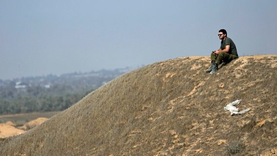 Ein israelischer Soldat sitzt auf einer Anhöhe nahe der Grenze zum Gazastreifen im Süden Israels. © AP/dpa Foto: Tsafrir Abayov
