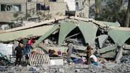 Palästinenser inspizieren die Trümmer einer Schule in Deir al-Balah im Gazastreifen, die bei einem israelischen Luftangriff zerstört wurde. © AP/dpa Foto: Abdel Kareem Hana