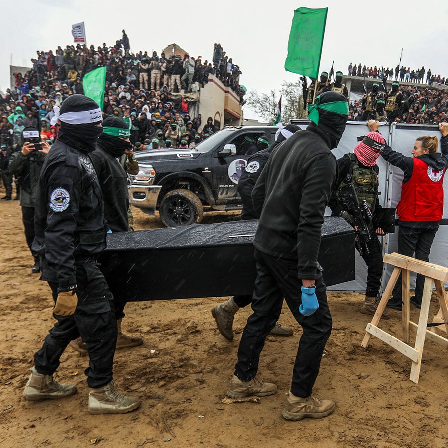 Vermummte Mitglieder der Terrororganisation Hamas tragen einen Sarg mit den sterblichen Überresten einer Geisel zur Übergabe an das Internationale Rote Kreuz (IKRK) in Chan Junis im südlichen Gazastreifen. © dpa Foto: Abed Rahim Khatib